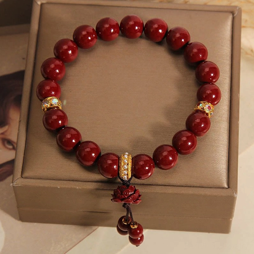 Cinnabar lotus bracelet displayed inside luxury brown jewelry gift box, featuring rich crimson beads, gold-rimmed crystals, and delicate lotus pendant
