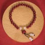 Cinnabar lotus prayer bracelet overhead view with deep red beads and white jade accents on wooden plate, perfect for Buddhist meditation and spiritual practice