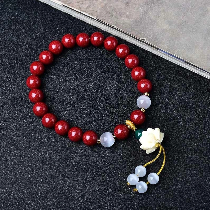 Side angle view of handmade cinnabar lotus bracelet on dark background, displaying bead arrangement and lotus pendant clarity