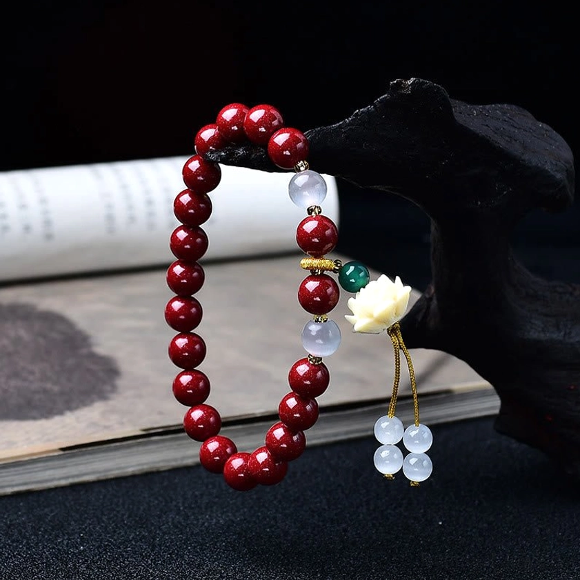 Two cinnabar Buddhist blessing bracelets with maroon beads and lotus pendants displayed on black wooden stand, showing design details and craftsmanship