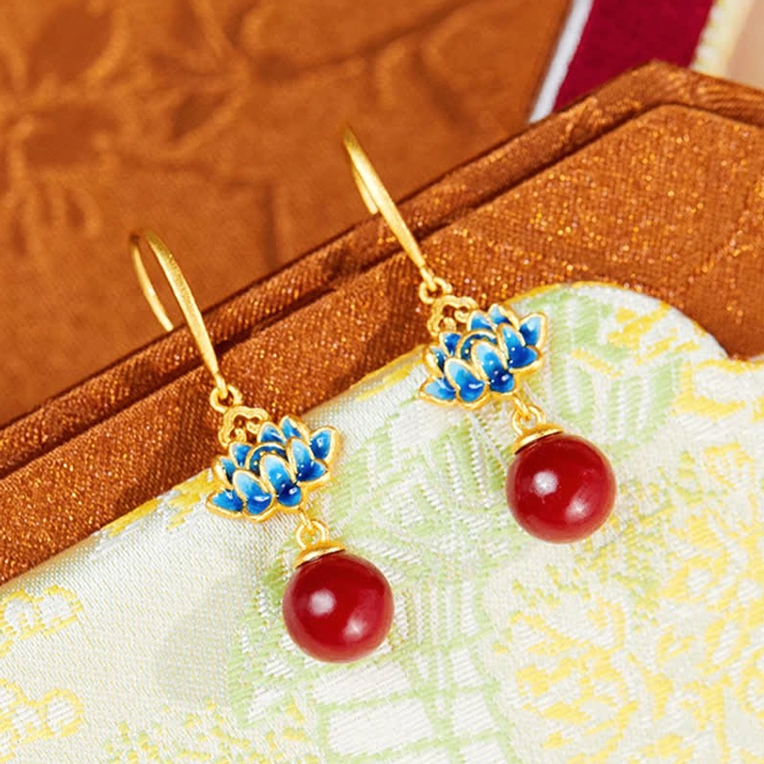 Handmade buddhist earrings featuring cinnabar beads and blue lotus enamel on traditional patterned cloth - oblique side view