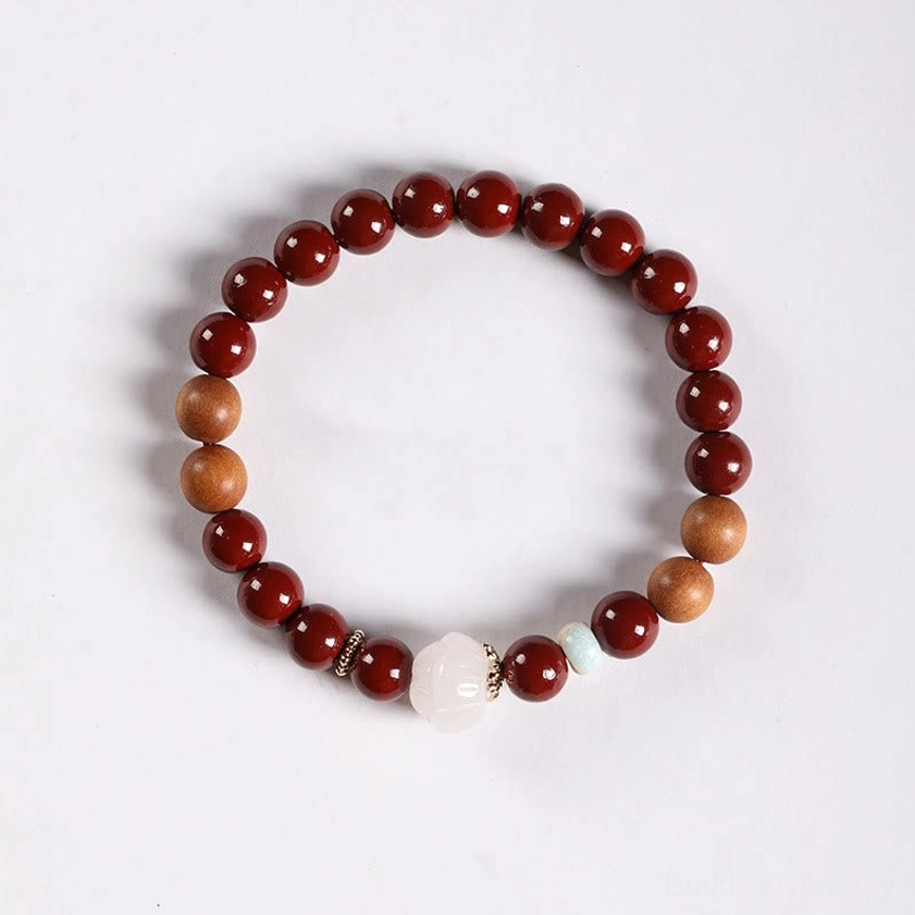 Buddhist blessing bracelet with cinnabar beads, white lotus charm, and mixed wood tones on minimalist light gray surface