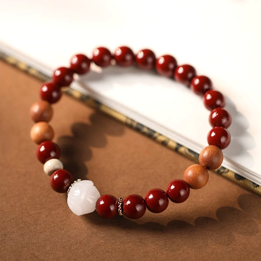 Sacred blessing bracelet with white lotus accent bead and cinnabar wood beads on warm brown background with book edge