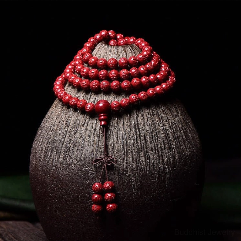 Carved cinnabar 108-bead mala displayed on dark ceramic vase with layered red beads and tassel drops