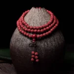 Carved cinnabar 108 mala beads bracelet with engraved Om Mani Padme Hum pattern, displayed on dark ceramic vase