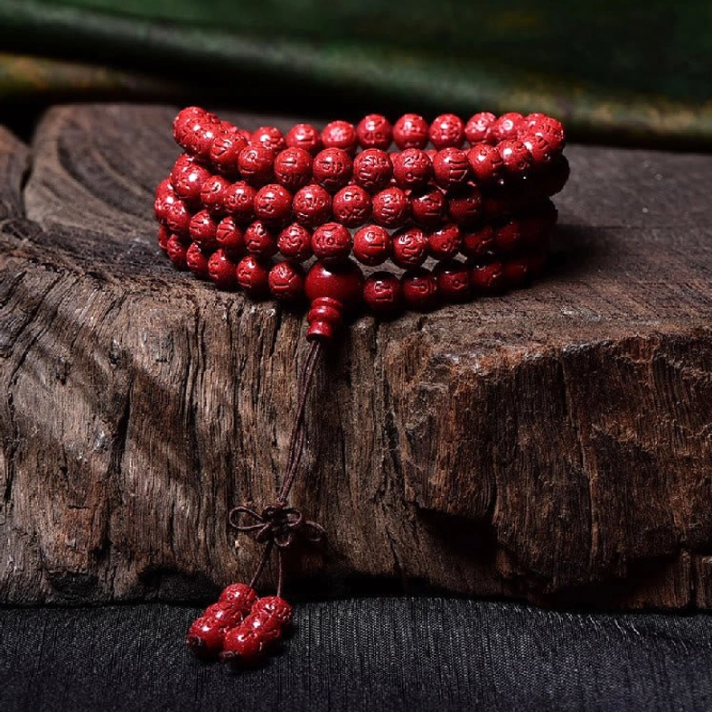 Stacked cinnabar mala bracelet with hand-carved red beads and Chinese knot tassel on wooden surface