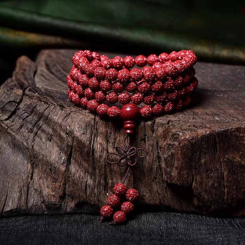 Stacked cinnabar mala bracelet with carved red beads and traditional Chinese knot tassel on wooden block
