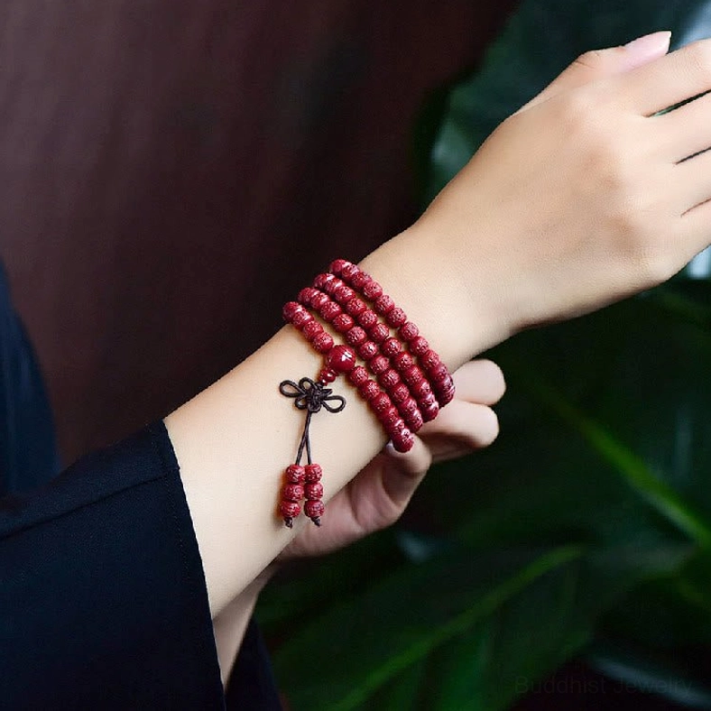 Worn cinnabar mala bracelet wrapped around wrist with multi-layered red beads and tassel pendant