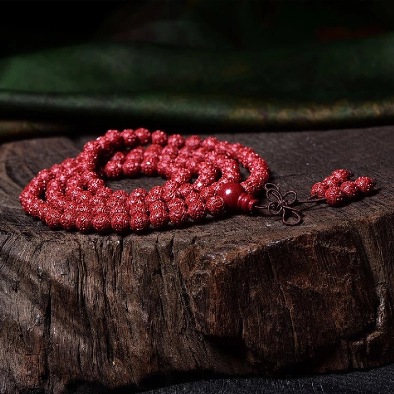 Cinnabar 108-bead mala with carved beads and decorative knot tassel on wooden stump