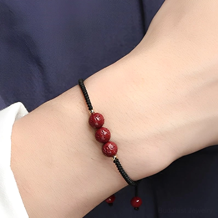 Black cord cinnabar Buddhist bracelet worn on wrist, close-up side view showing carved mantra beads and adjustable design on dark fabric
