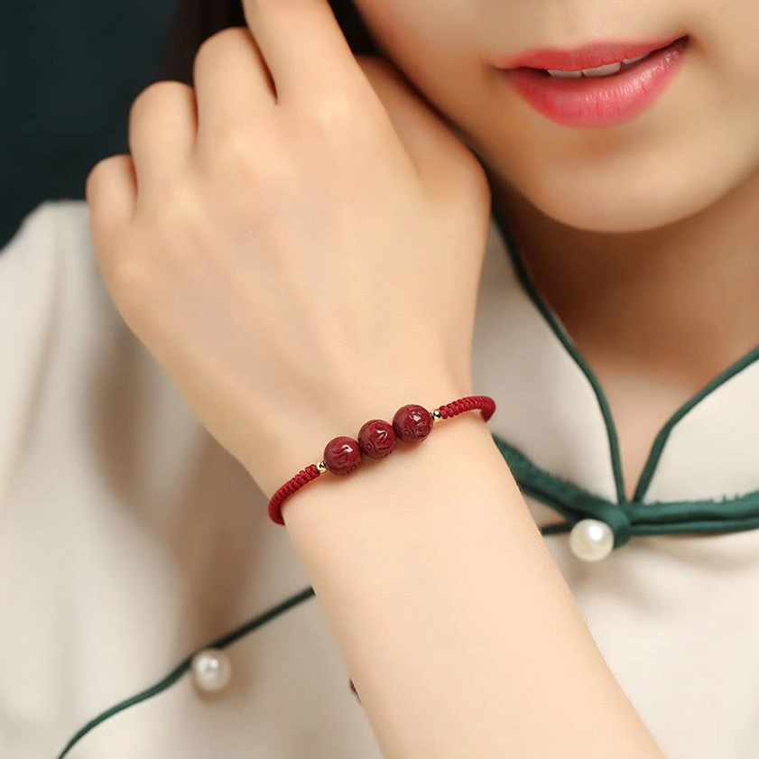 Buddhist mantra bracelet worn on wrist with traditional cheongsam, close-up side view showing red braided cord and three engraved cinnabar beads