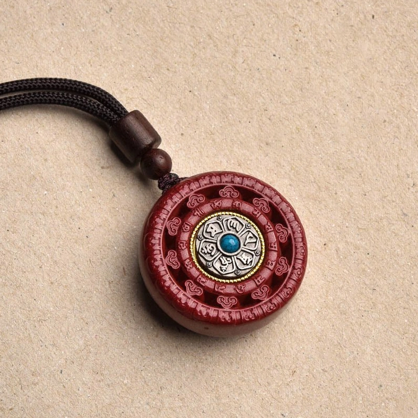 Close-up front view of red cinnabar Buddhist pendant with silver inlay and turquoise stone detail