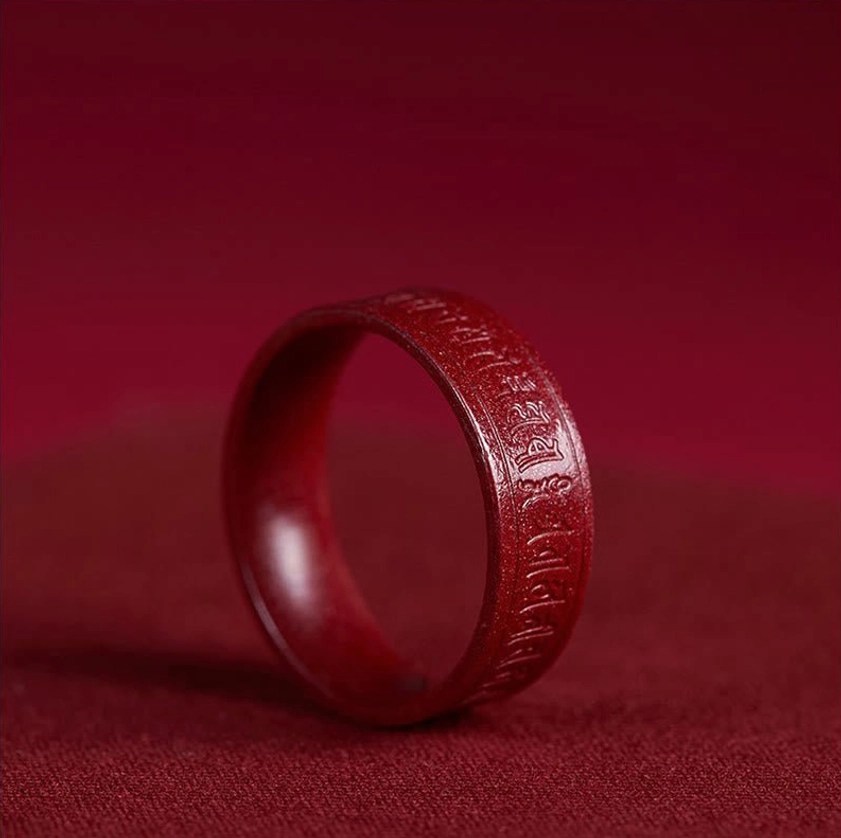 Cinnabar Buddhist mantra ring with laser-engraved script three-quarter side view showing clear engraving on dark red fabric