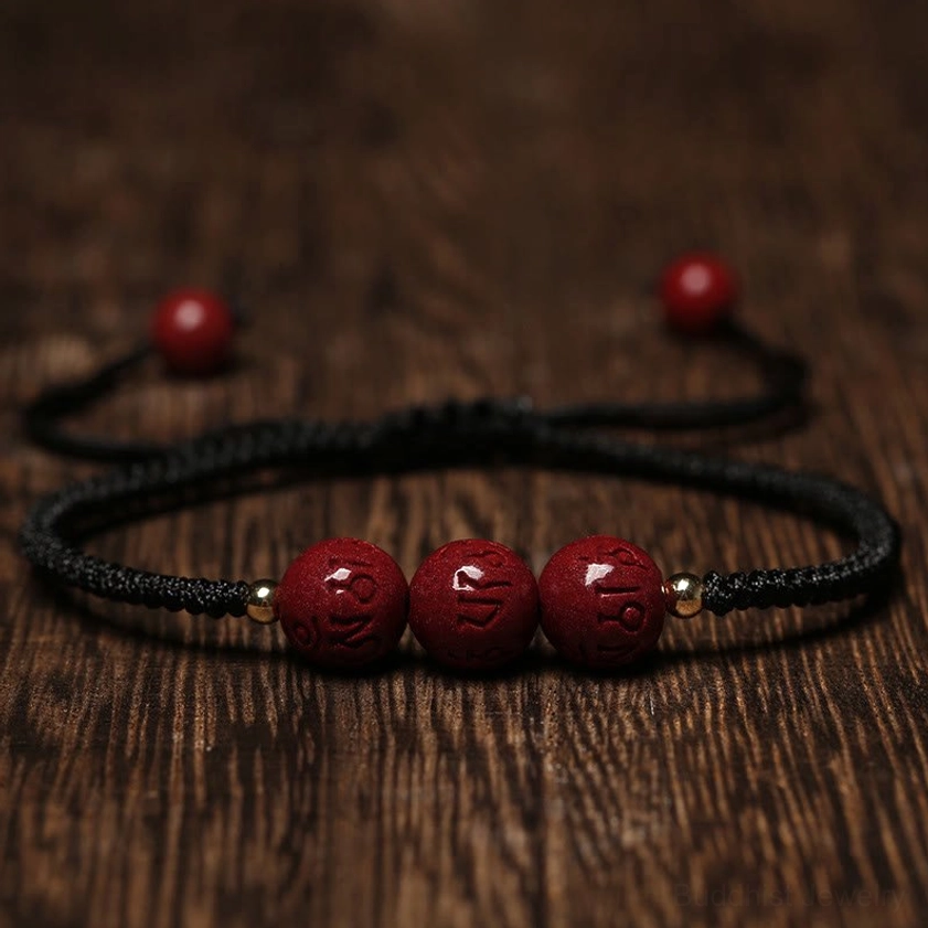 Handmade cinnabar Om Mani Padme Hum bracelet with black braided cord flat lay on wooden surface, showing carved mantra beads and adjustable pull knot