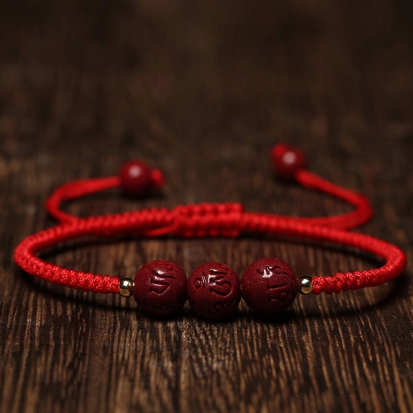 Handmade cinnabar Om Mani Padme Hum braided bracelet with bright red cord flat lay on wooden surface, showing adjustable pull design and carved spiritual beads