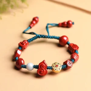 Cinnabar Buddhist string bracelet with Om Mani Padme Hum beads, teal braided cord, and gourd-shaped cinnabar charm on light background