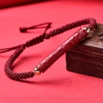 Handmade cinnabar Om Mani Padme Hum Buddhist blessing bracelet with red braided cord and gold accents, flat lay shot