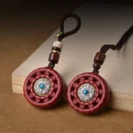 Cinnabar Om Mani Padme Hum rotating Buddhist pendant displayed on wooden desk with woven lanyard