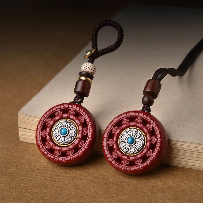 Cinnabar Om Mani Padme Hum rotating Buddhist pendant displayed on wooden desk with woven lanyard