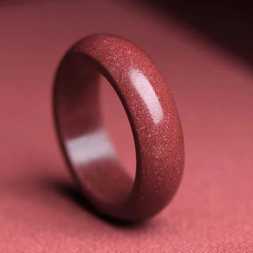 Close-up view of smooth polished cinnabar ring showing natural reddish-brown crystalline texture and matte finish on fabric surface