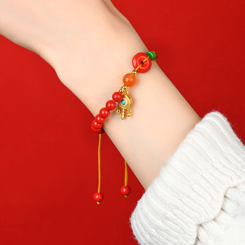 Buddhist bracelet worn on forearm with white sweater sleeve, side angle view displaying adjustable tassel with red beads