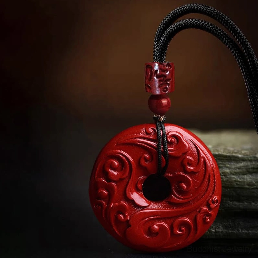 Cinnabar peace buckle necklace with cloud pattern carved pendant displayed on stone base, showing side profile and braided black cord construction