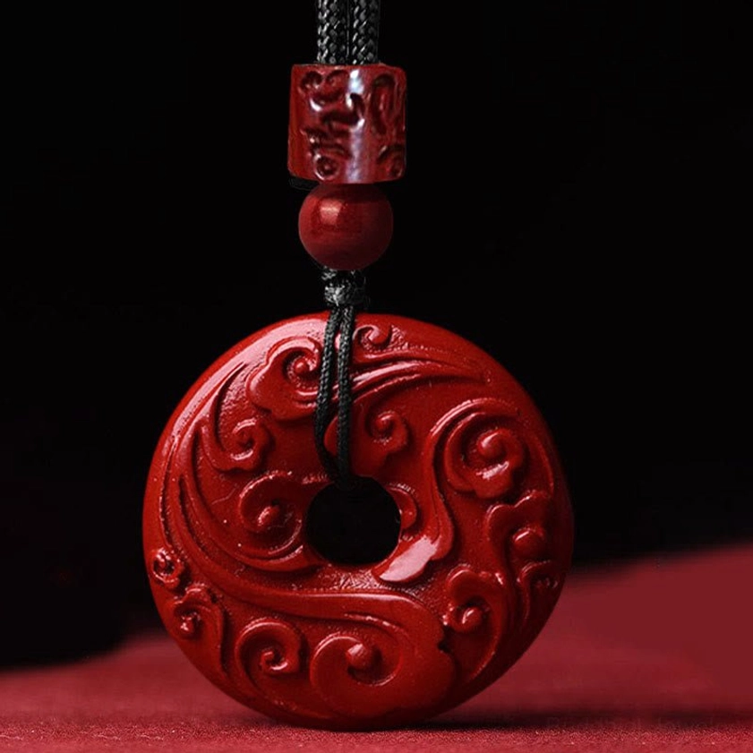 Close-up detail of handcrafted cinnabar peace buckle pendant with intricate cloud relief carving and glossy deep red natural mineral surface