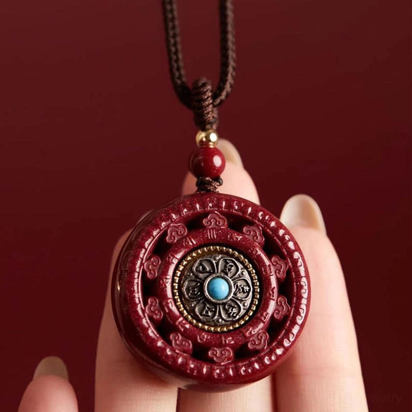 Hand-held detail of carved cinnabar pendant showing intricate mantra patterns and blue stone inlay