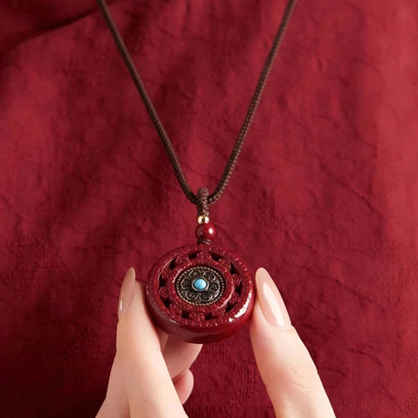 Close-up of hand holding cinnabar Buddhist pendant showing detailed carving and metalwork
