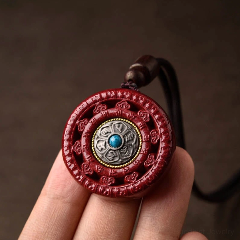 Finger-held view of red cinnabar pendant displaying carved texture and turquoise stone inlay