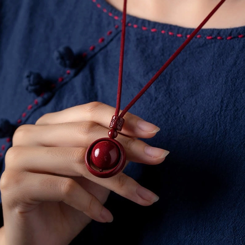 Cinnabar om mani padme hum pendant necklace held by hand wearing traditional embroidered navy blue clothing