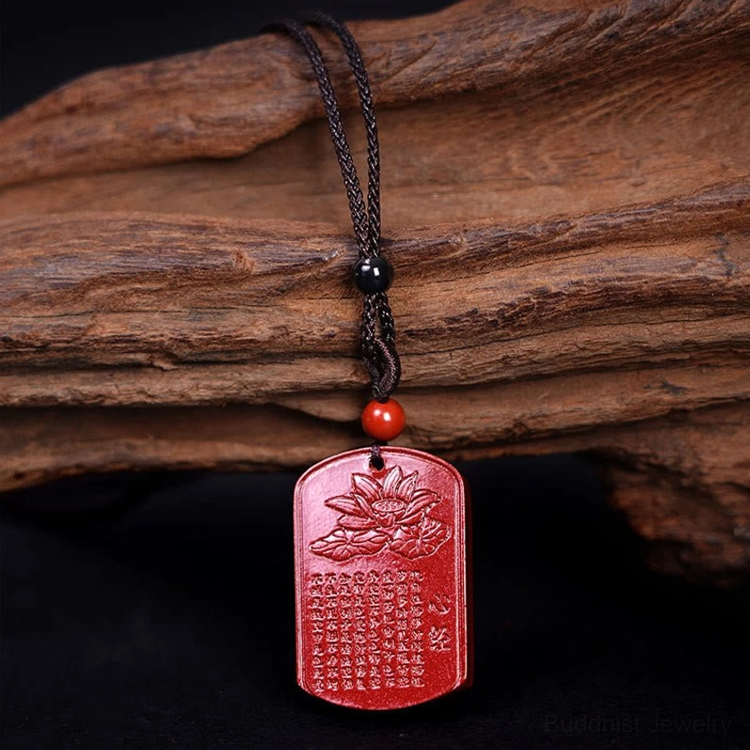 Red cinnabar Buddhist prayer pendant hanging on black woven cord side view
