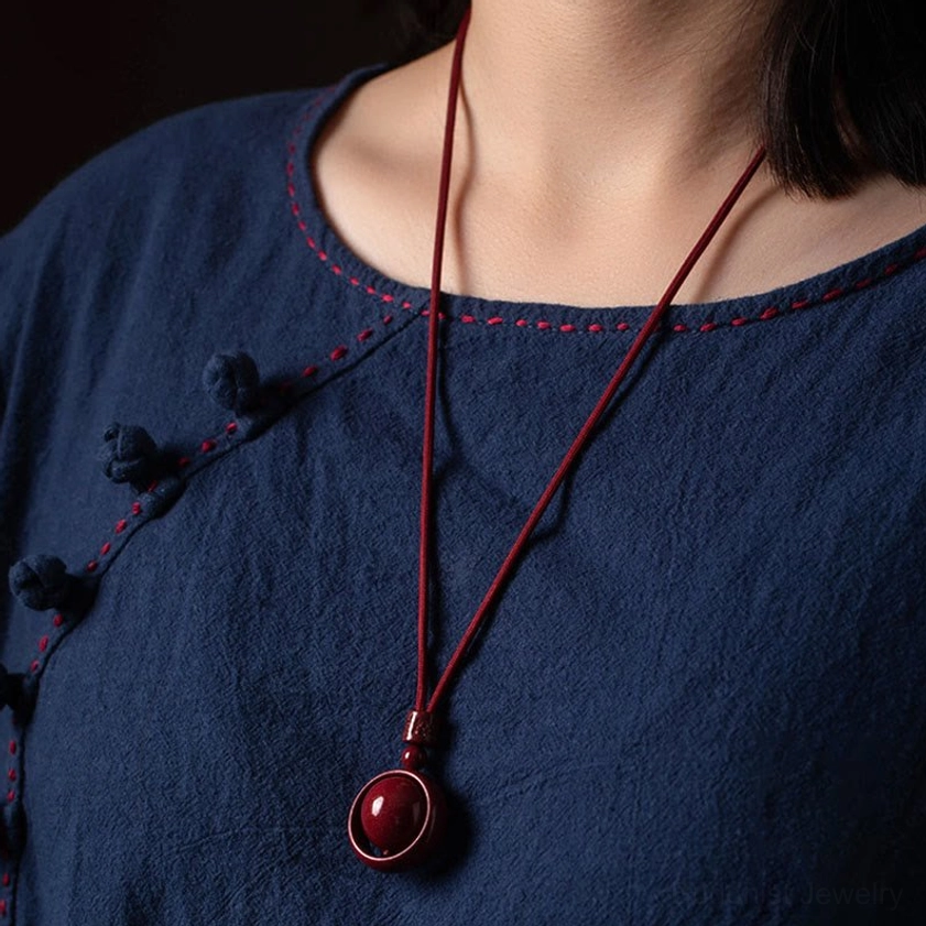 Cinnabar pendant necklace worn on model neck with long red cord, casual indoor studio setting