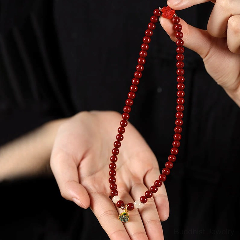 Close-up hand-held view of cinnabar prayer bead bracelet showing detailed enamel lotus pendant