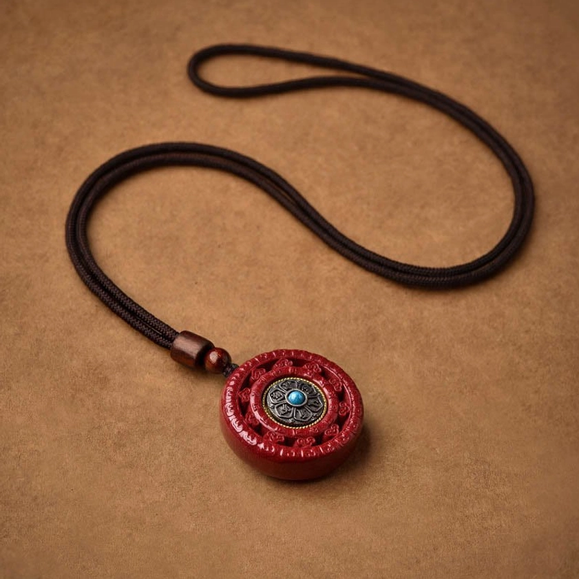 Rotating cinnabar pendant close-up showing Om Mani Padme Hum mantra engraving and inlay work
