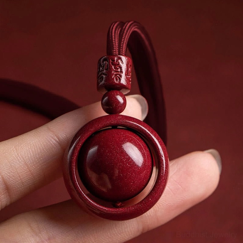 Speckled cinnabar round bead pendant held on finger showing carved top decorative bead and hollow ring frame