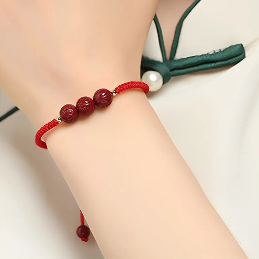 Red cord cinnabar spiritual bracelet worn on wrist with decorative accessory, close-up side view showing hand-braided construction and mantra beads