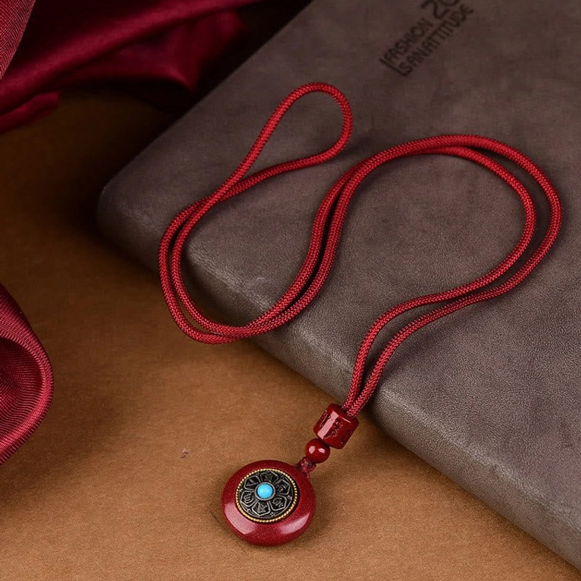 Cinnabar Om Mani Padme Hum necklace with turquoise inlay flat lay on leather backdrop
