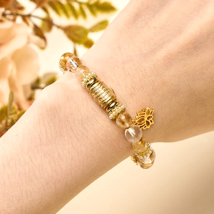 Woman wearing citrine and clear quartz lotus bracelet on wrist with natural foliage background