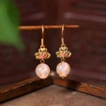 Citrine lotus enamel drop earrings with pink crystal beads and gold ear hooks, front hanging view on dark wood background