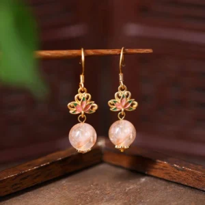 Citrine lotus enamel drop earrings with pink crystal beads and gold ear hooks, front hanging view on dark wood background
