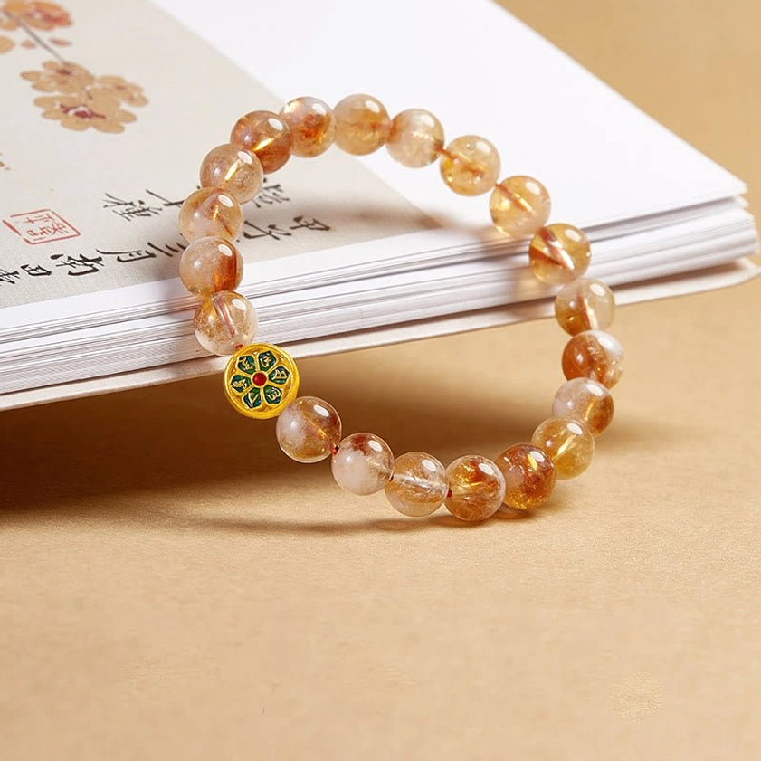 Buddhist citrine prayer bracelet with gold-trimmed enamel OM charm displayed on stacked books with tan background