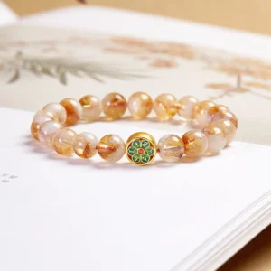 Citrine Om Mani Padme Hum sterling silver bracelet flat lay on Chinese book, showing natural citrine beads with enamel decorated charm