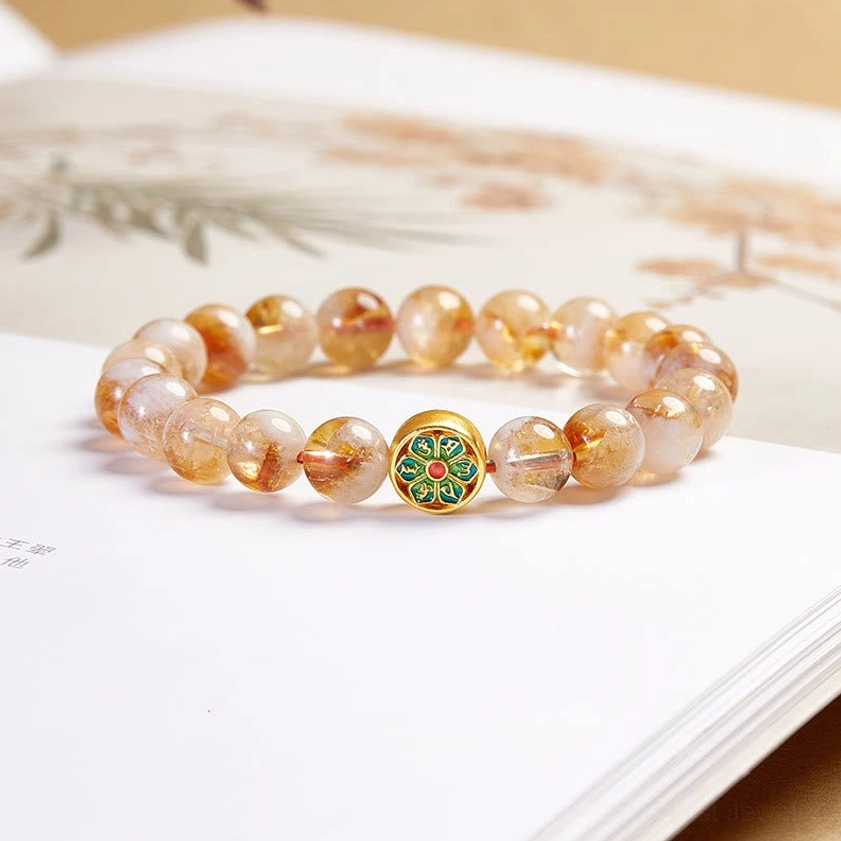 Citrine Om Mani Padme Hum sterling silver bracelet flat lay on Chinese book, showing natural citrine beads with enamel decorated charm