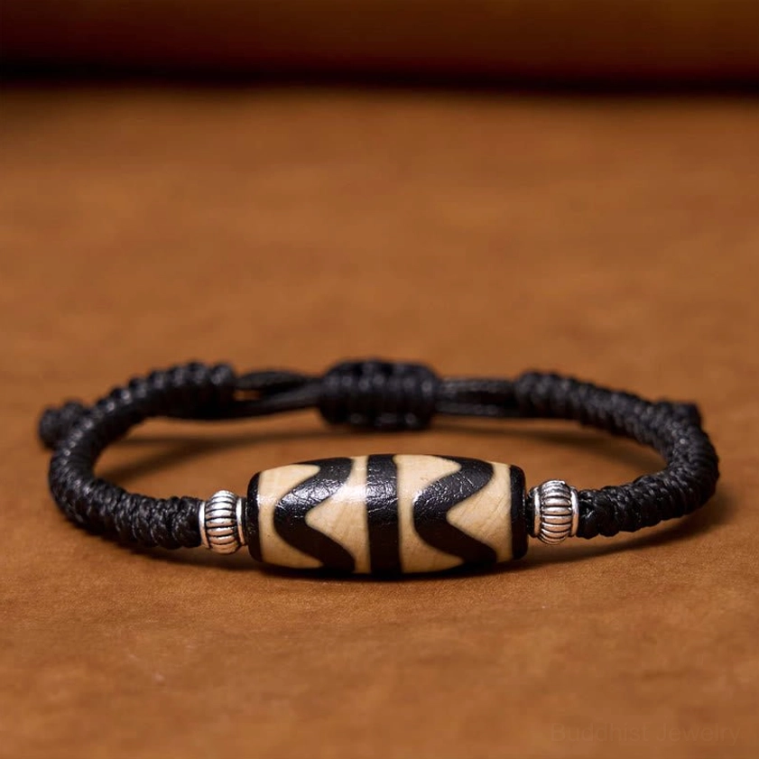 Classic dzi bead bracelet flat lay view featuring hand-painted pattern with black elastic cord and silver spacers