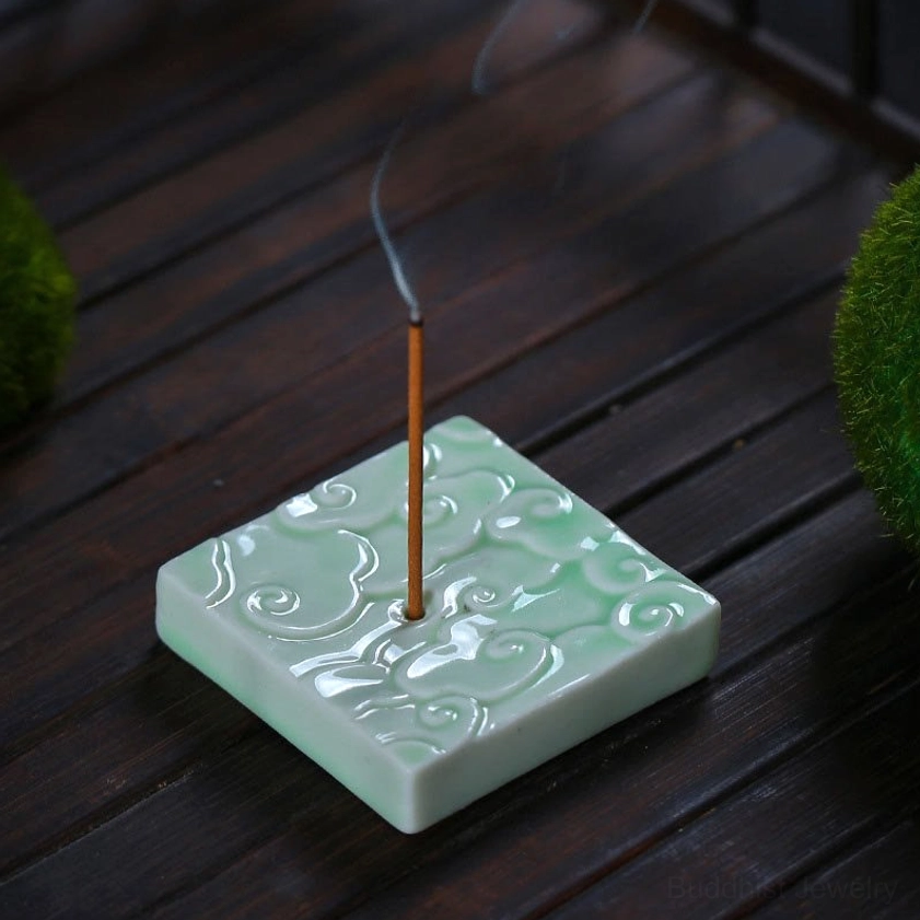 Celadon square cloud incense burner on wooden tabletop with lit incense burning, showing neat embossed cloud design and rising fragrant smoke