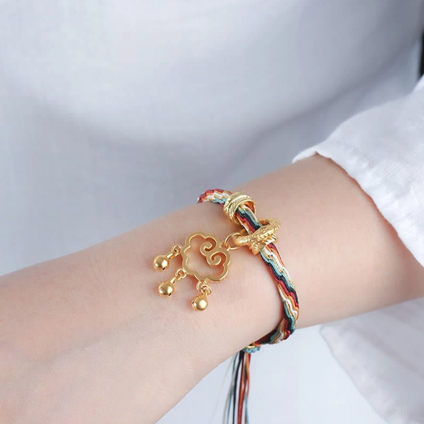 Wrist-wearing view of handmade auspicious cloud lock bracelet with multicolor woven cord, gold hardware and hanging tassel on white fabric background
