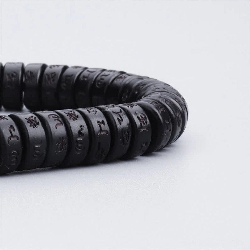 Macro close-up of coconut shell bracelet beads showing hand-engraved sacred mantras on black disc beads