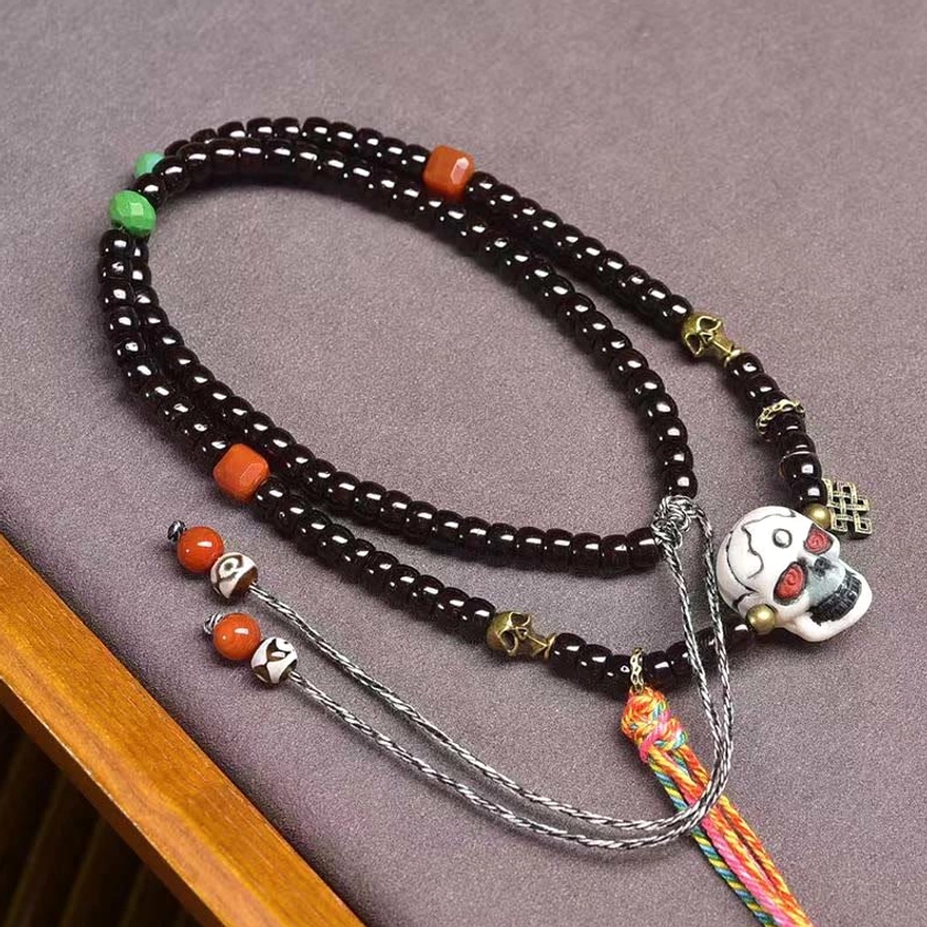 Overhead view of Buddhist coconut shell bracelet with orange accent beads and metal charms on gray mat