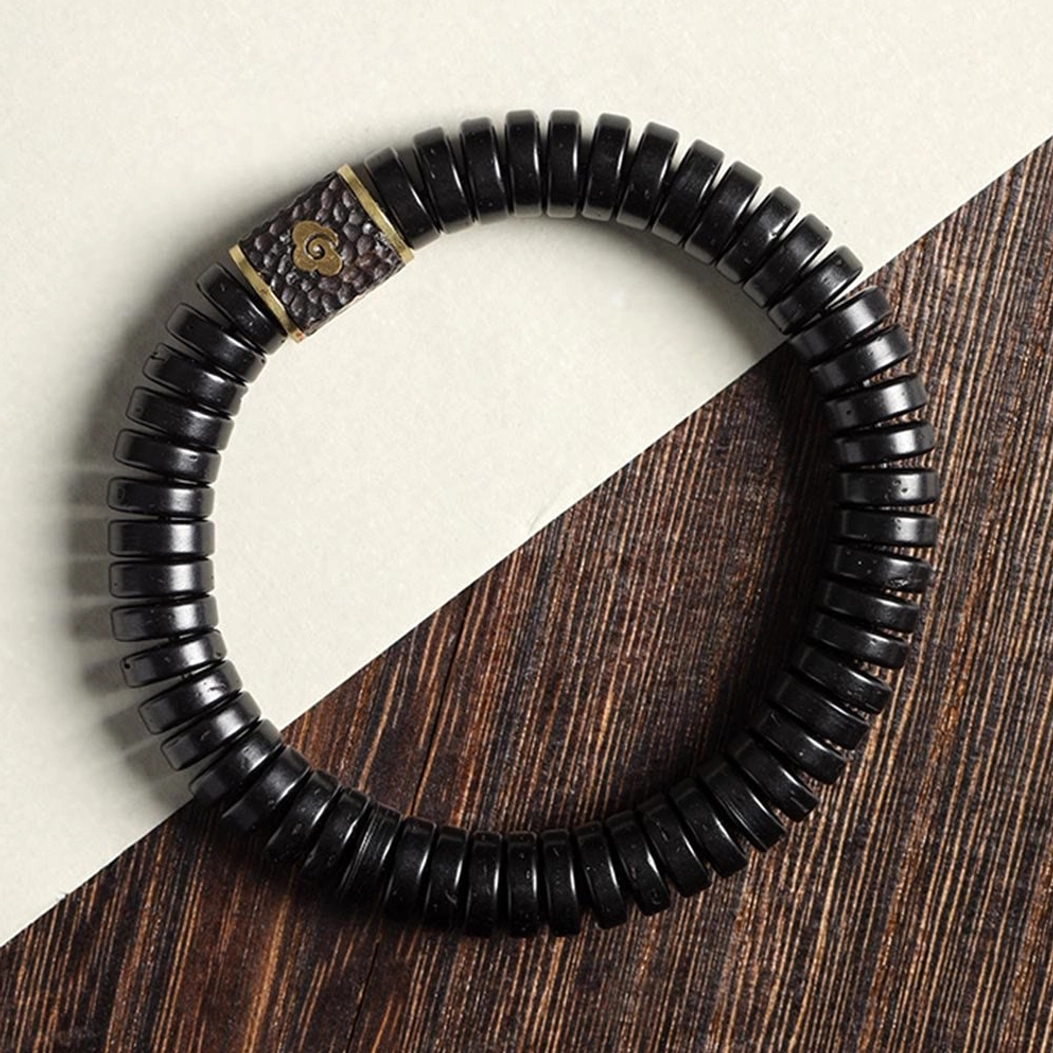 Buddhist coconut shell bracelet flat lay featuring engraved cloud metal accent on wooden and neutral background